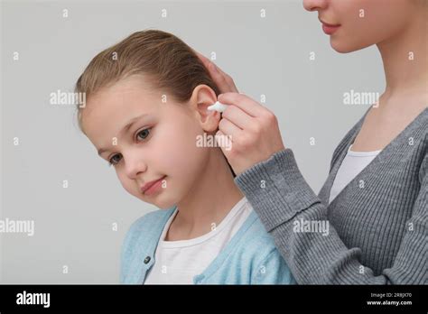 Mother Dripping Medication Into Daughters Ear On Light Grey Background