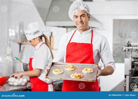 Cocinero Sonriente Holding Small Pizzas En El Molde Para El Horno Foto