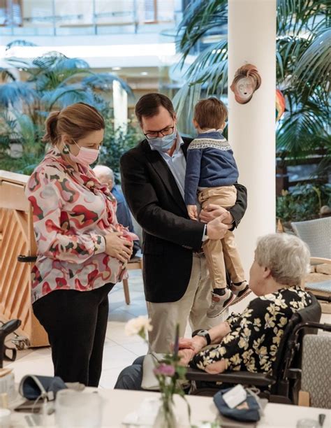 A Man In A Suit And Tie Holding A Baby While Standing Next To An Older