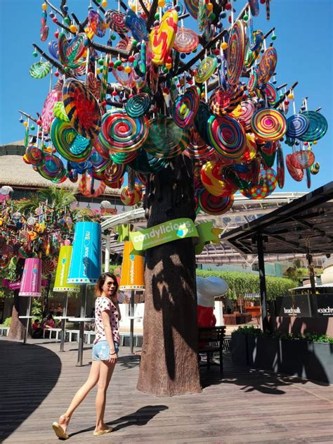 A Woman Walking Past A Tree With Many Colorful Objects On It