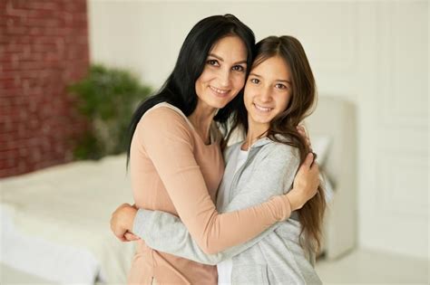 Feliz madre latina e hija abrazándose sonriendo a la cámara mirando cariñosa mientras posan