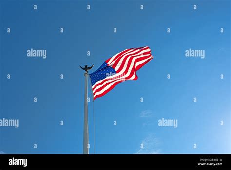 The American Flag Flapping In The Wind Against A Blue Sky With Wispy