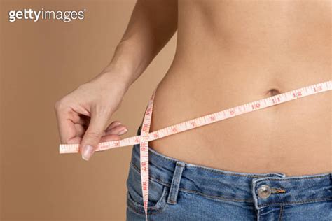 Female Naked Belly With Tape In Hands Measuring Waistline With Blue