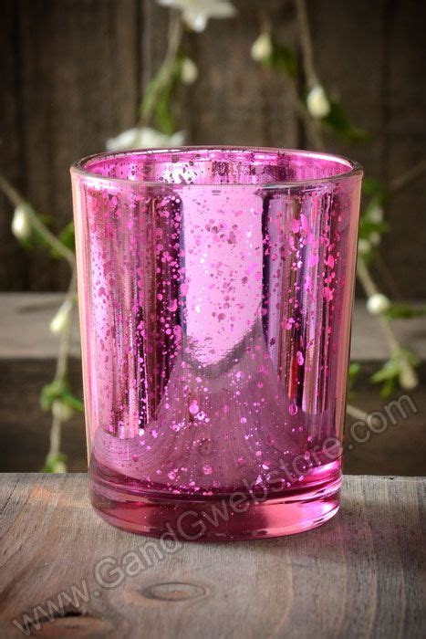 A Pink Glass Candle Holder Sitting On Top Of A Wooden Table With Flowers In The Background