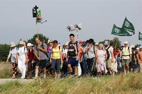 a group of people walking down a dirt road with flags in the air and onlookers behind them