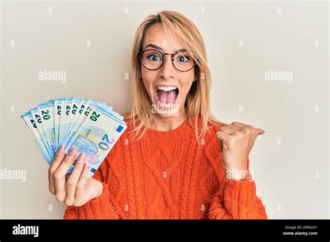 Belle femme blonde portant billets en euros pointant du pouce vers le haut sur le côté