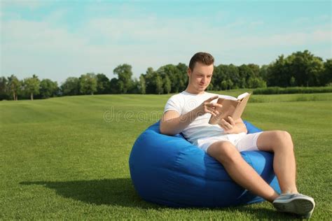 Young Man Reading Book While Sitting On Bean Bag Chair Outdoors Stock