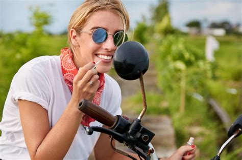 La motociclista rubia de moda usa sombras pinta los labios con lápiz