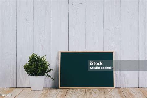 Blank Green Chalkborad With Wood Frame And Little Decorative Tree In White Vase On Wooden Table