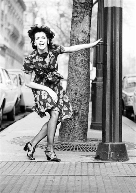 A Black And White Photo Of A Woman Leaning On A Pole With Her Arms