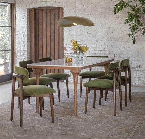 A Dining Room Table With Green Chairs And A White Brick Wall In The