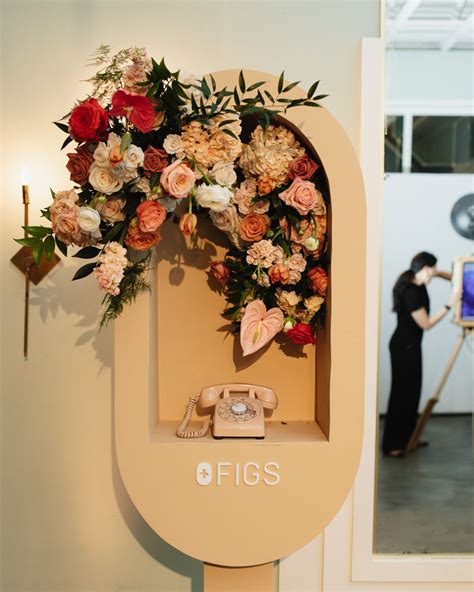 A Woman Taking A Photo In Front Of A Phone Booth With Flowers On The Wall