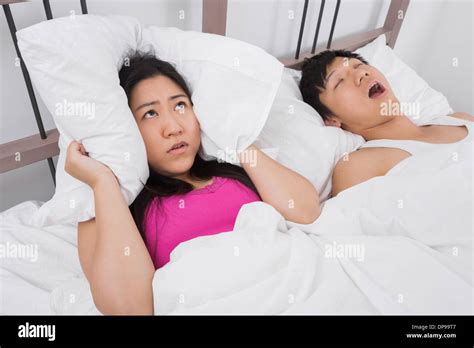 Frustrated Woman Covering Ears With Pillow While Man Snoring In Bed