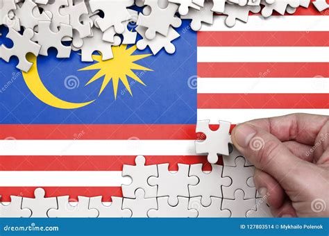 Malaysia Flag Is Depicted On A Table On Which The Human Hand Folds A