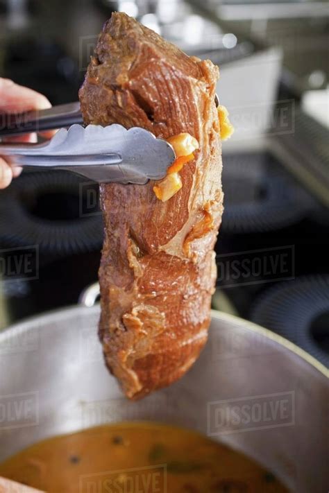 A Hand Holds A Tenderloin Beef Above A Pot With Pieces Of Carrots And