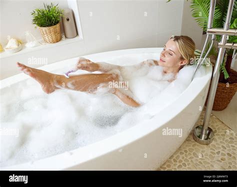 Beautiful Woman Shaving Leg With Razor In Bathtub With Foam Relaxation And Taking Care Stock