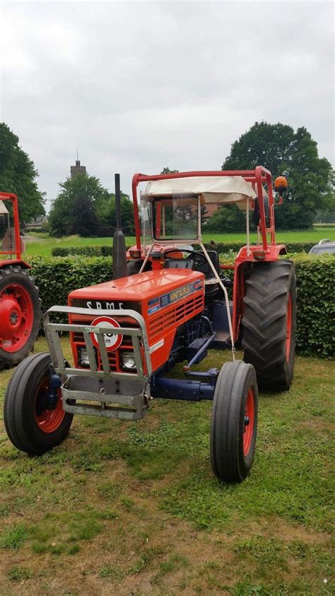 Two Farm Tractors Parked In The Grass Next To Each Other On A Field