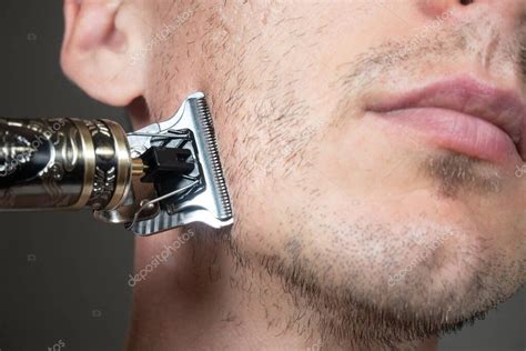 El hombre está cortando la barba por la máquina de afeitar eléctrica de