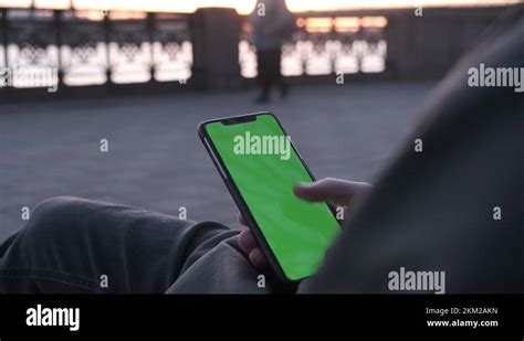 A Young Man Sitting And Scrolling His Phone With A Green Screen Close