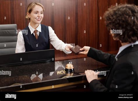 Happy Young Hotel Staff Looking At Client Passing Her Document Over