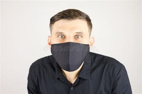 A Man In A Black Medical Mask Looks At The Camera On A White Background