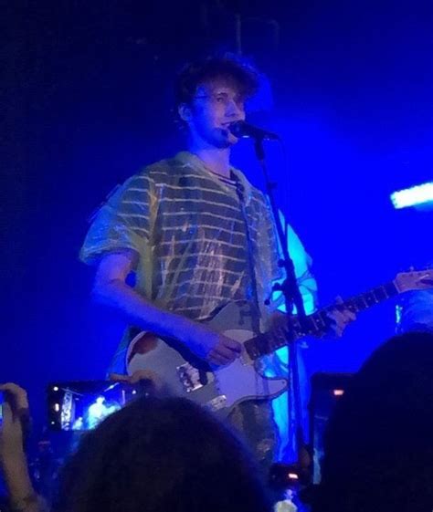 A Man With A Guitar Standing In Front Of A Microphone And Some People