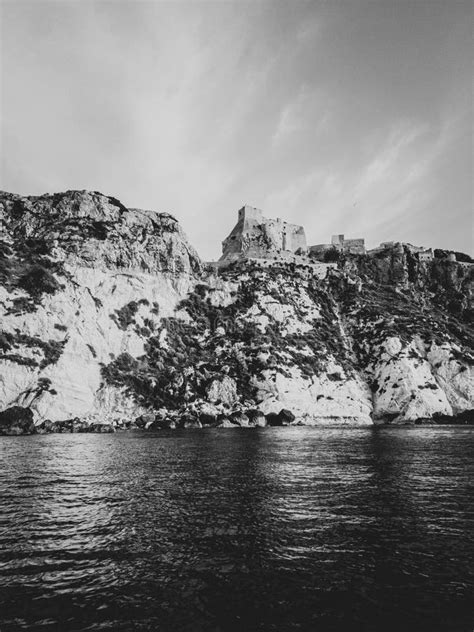 Vertical Grayscale Shot Of Castle Ruins On A Cliff Over Water At The