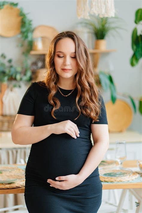 Beautiful Pregnant Woman In Black Dress Touches The Stomach In The Home