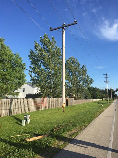 An Electric Pole In The Middle Of A Grassy Area Next To A Road And Fence