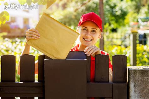 smiling postman mail carrier inserting envelope into mailbox 이미지