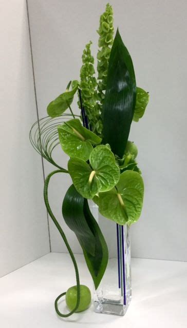 A Glass Vase Filled With Green Plants And Greenery On Top Of A White Table