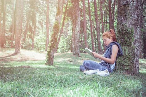 Premium Photo Young Woman Reading Book While Sitting By Tree Trunk In