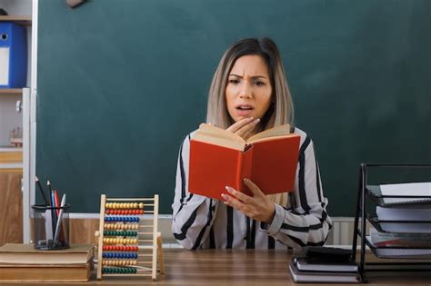 Jeune femme enseignante assise au bureau de l école devant le tableau