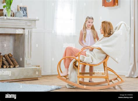 Young Mother Sitting In Rocking Chair And Her Little Daughter Standing