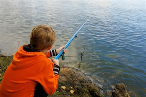 El niño está pescando con una caña de pescar en el río sosteniendo una