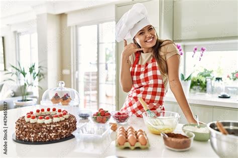 Beautiful Young Brunette Pastry Chef Woman Cooking Pastries At The Kitchen Smiling Doing Phone