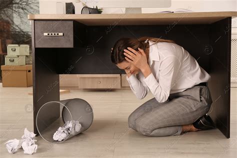 Scared Young Woman Hiding Under Office Desk During Earthquake Stock