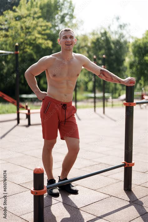 Full Body Of Smiling Muscular Male Athlete With Naked Torso Standing On Sports Ground After