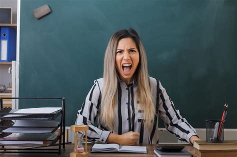 Jeune femme enseignante assise au bureau de l école devant le tableau