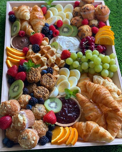 A Platter Filled With Croissants Fruit And Pastries On Top Of Green Grass