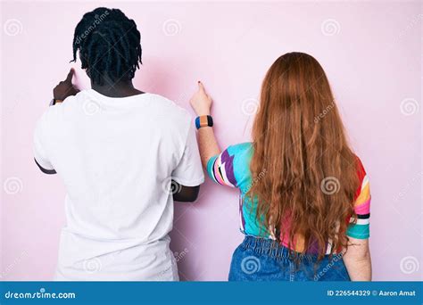 Interracial Couple Wearing Casual Clothes Posing Backwards Pointing