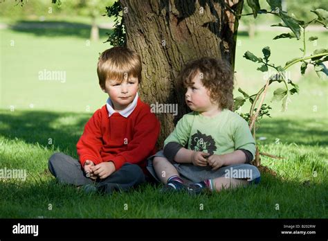 Dos niños sentados bajo un árbol en un parque Fotografía de stock Alamy