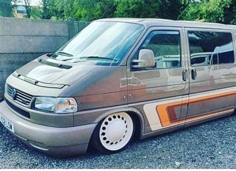 A Van Parked On Gravel With Trees In The Backgrouund And Concrete Wall