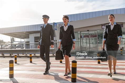 Two Flight Attendants With Bags And Their Colleague Crossing The Road