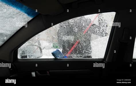 Closeup of frozen car window - view from inside the car. Man clears car ...