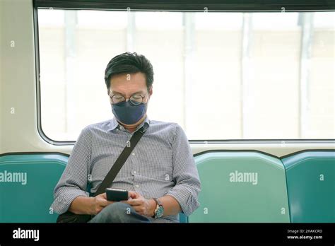 Asian Man Commuter Wearing Face Mask Looking At His Smartphone Sitting