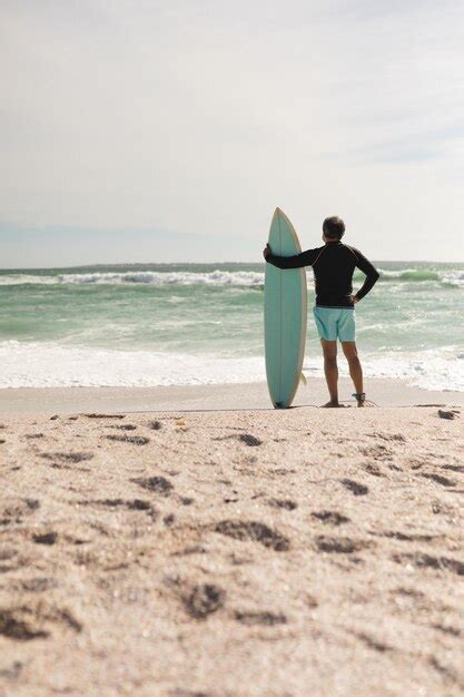 Vista traseira do homem sênior biracial em pé prancha de surf na