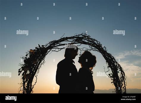 Silhouettes Of Hugging Bride And Groom Near The Wedding Arch At Sunset