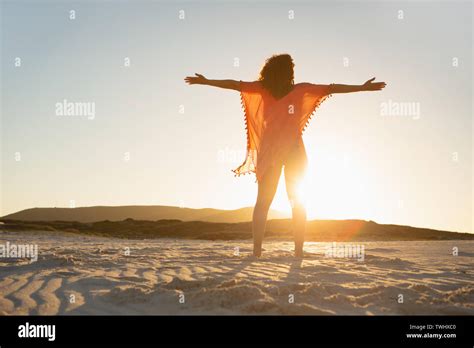 Woman With Arms Stretched Out Standing On Beach In The Sunshine Stock