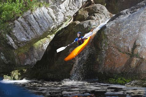 Mid adult man kayaking down river waterfall stock photo